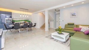 A modern living room with a dining area, a green sofa, and a staircase leading to another level. - Holiday home with pool for 8 people (Malinska)