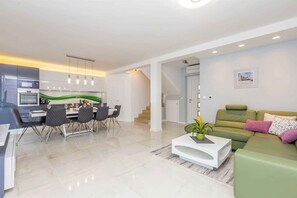 A modern living room with a dining area, a green sofa, and a staircase leading to another level.