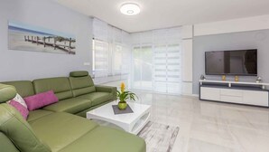 A modern living room with a green sofa, a coffee table with a plant, a flat-screen TV, and a large window with blinds. - Holiday home with pool for 8 people (Malinska)