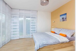Une chambre à coucher avec un lit, une fenêtre avec des stores, un tableau au mur et un luminaire au plafond.
