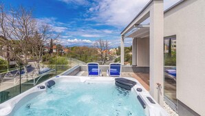 A hot tub with two blue chairs, surrounded by a glass railing, overlooking a residential area with trees and houses. - Holiday home with pool for 8 people (Malinska)