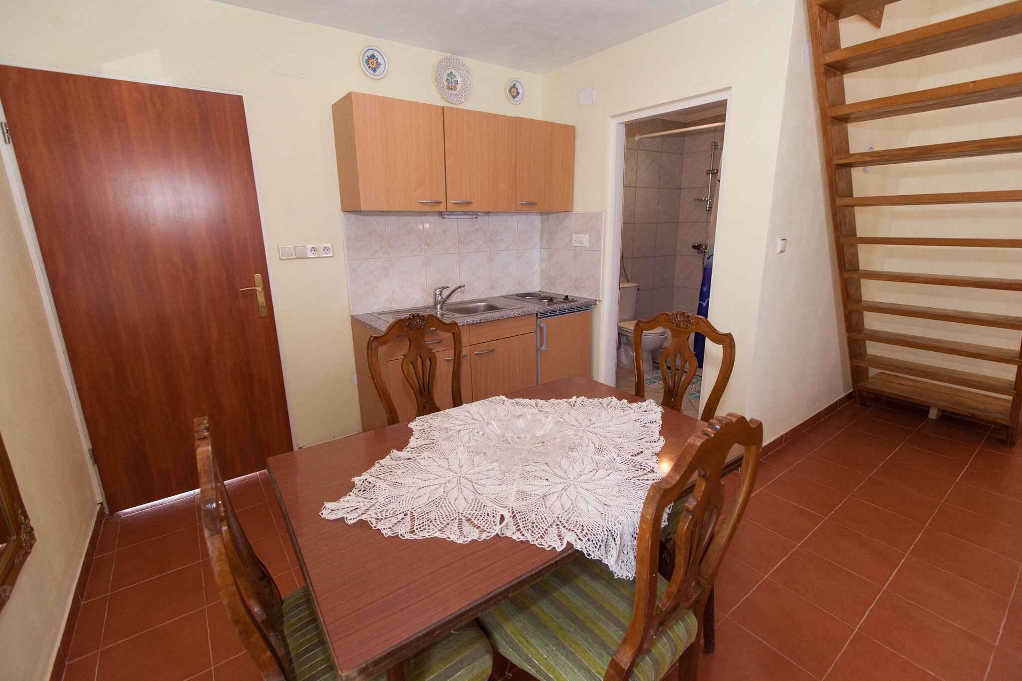 Uma área de jantar com mesa de madeira, cadeiras e uma cozinha ao fundo.