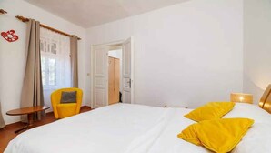 A hotel room with a large bed, a small table, a yellow chair, and a door leading to another room. - Villa with pool for 8 people (Grižane)