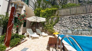 A poolside area with a stone patio, lounge chairs, a table, and a pool. - Villa with pool for 8 people (Grižane)