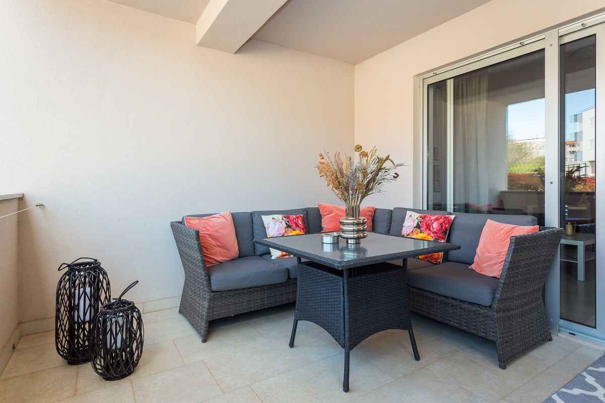 Un balcon agrémenté d’un canapé en osier foncé, d’une petite table sur laquelle est posé un vase de fleurs séchées, et de deux lanternes noires.