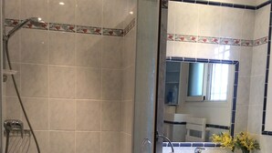 Ein Badezimmer mit einer Duschkabine, einem Waschbecken mit Spiegel darüber und einem Handtuch an der Tür.