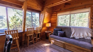 A cozy cabin interior with a wooden floor, a sofa with cushions, a lamp, and a table with chairs. - Enjoy a cozy cabin near the lake! Sleeps 8,  4 Beds. (Panguitch Lake)