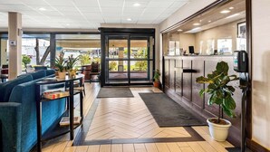 Un hall d’hôtel moderne doté d’un comptoir d’accueil, d’un espace salon et de grandes fenêtres offrant une vue sur l’extérieur.