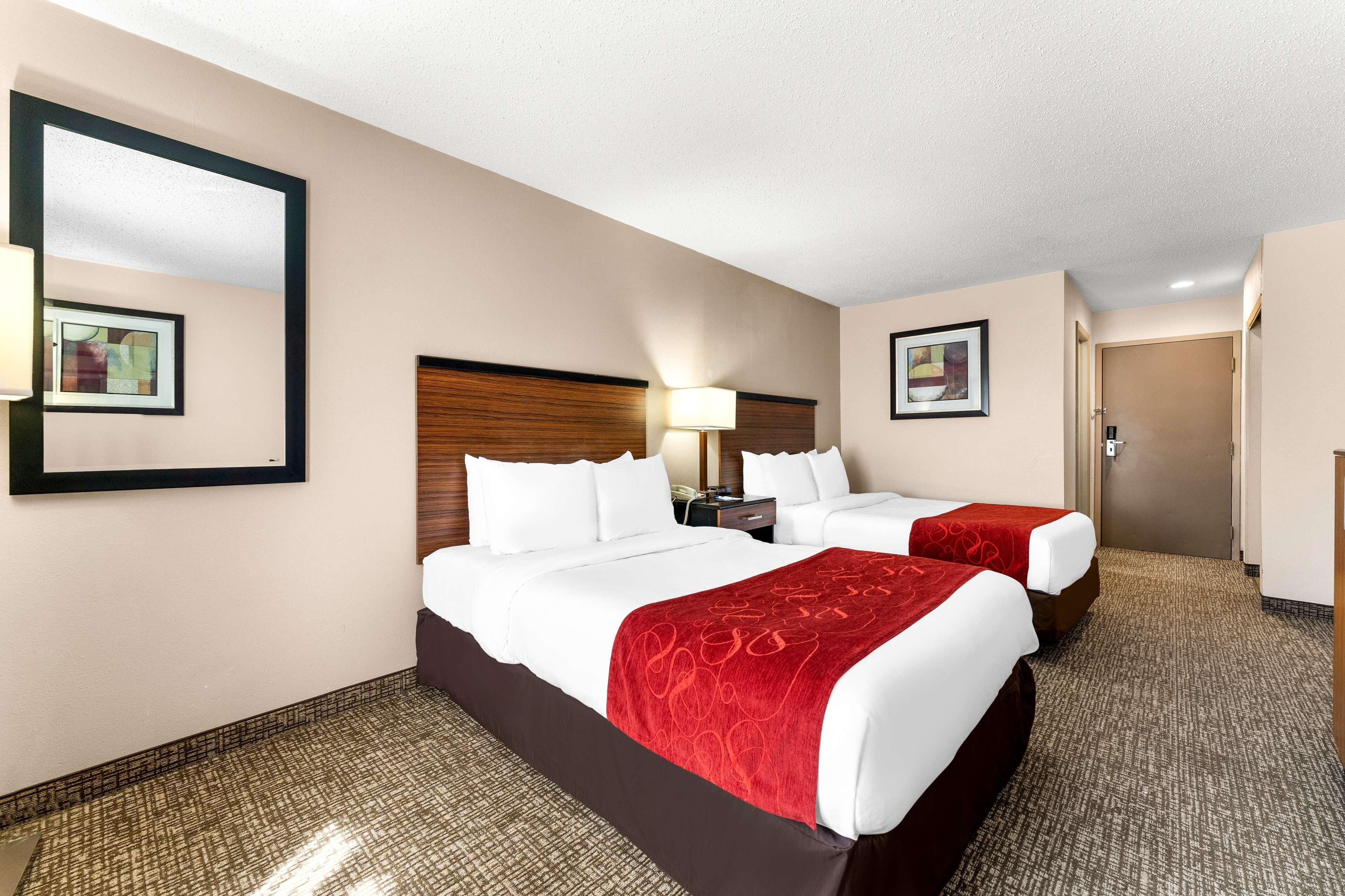 A hotel room with two beds, a nightstand, a lamp, and a door.