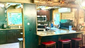 Une cuisine avec des meubles de rangement en bois, un réfrigérateur en acier inoxydable, un four à micro-ondes et un évier. On y trouve trois tabourets avec des coussins rouges.
