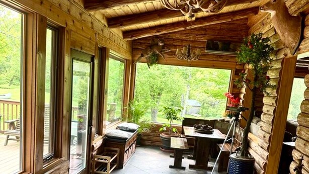 L’intérieur d’une cabane en rondins, avec un sol carrelé en pierre, des meubles en bois et une grande fenêtre donnant sur un paysage verdoyant.