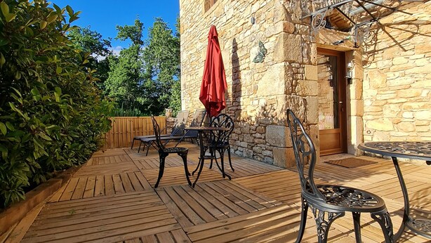 An outdoor patio with wooden flooring, stone walls, and metal furniture. - Chambre d'hôte Opale - Refinement, serenity and well-being guaranteed (Puy-l'Évêque)
