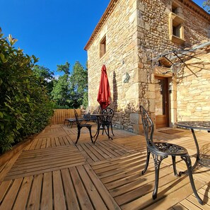 An outdoor patio with wooden flooring, stone walls, and metal furniture. - Chambre d'hôte Opale - Refinement, serenity and well-being guaranteed (Puy-l'Évêque)