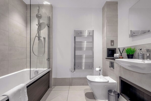 A modern bathroom with a glass-enclosed shower, a standalone bathtub, a toilet, and a sink with a mirror above. - Two Bedroom Apartment in Hackney Wick (London)