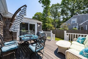 Une terrasse avec une table et des chaises, un espace salon couvert et une vue sur la maison.