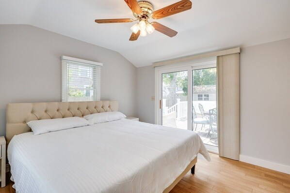 Une chambre avec un grand lit, un ventilateur de plafond, une fenêtre avec des stores et une vue sur l’extérieur.