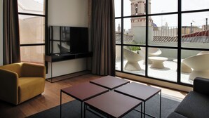 Una camera d'albergo moderna con un'ampia finestra, una TV a schermo piatto, un divano, due tavolini e una poltrona.