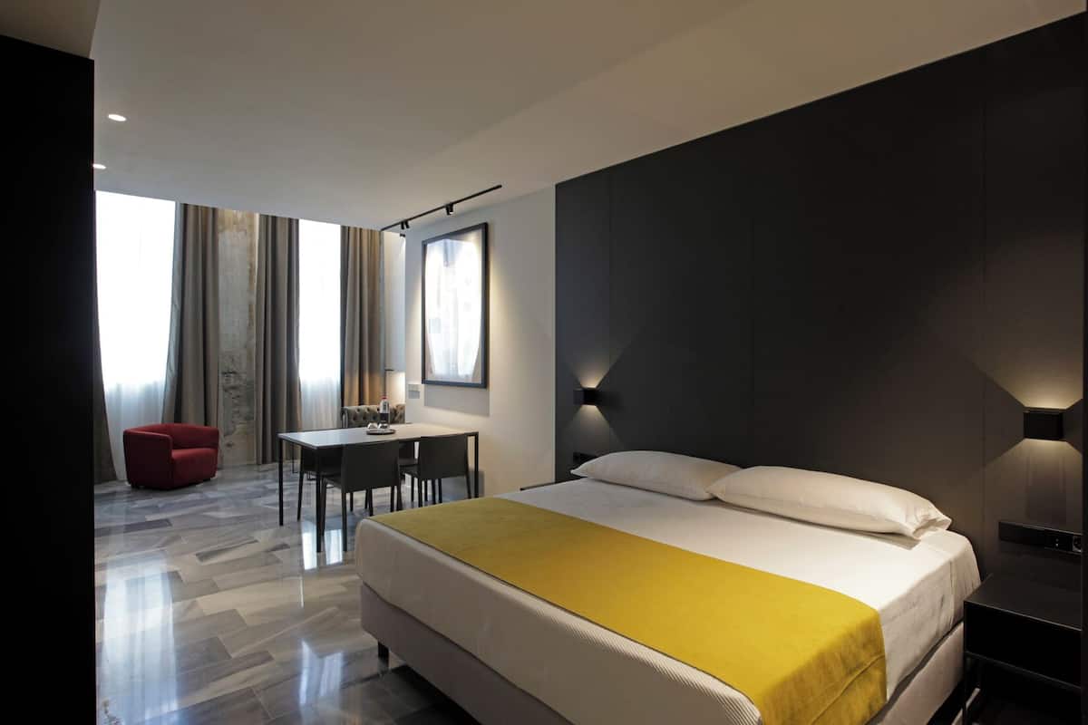 A modern hotel room with a large bed, a desk, and a red chair.