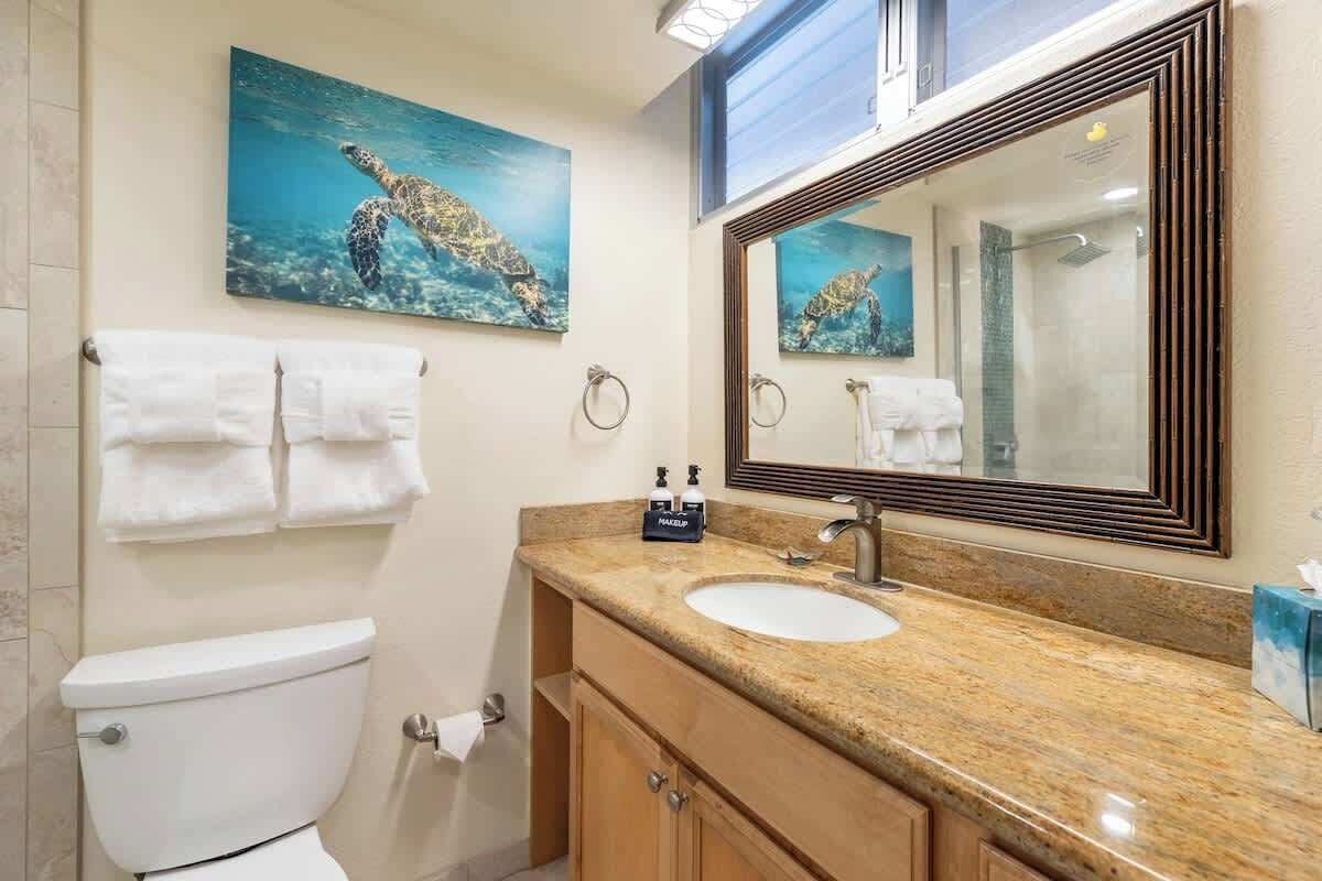 Een badkamer met toilet, wastafel, spiegel en een schilderij van een zeeschildpad.