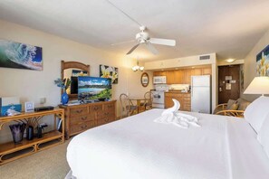 Une chambre d’hôtel équipée d’un lit, d’un bureau, d’une télévision, d’une kitchenette et d’un ventilateur de plafond.