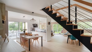 Eine moderne Küche mit Essbereich, einer Treppe und großen Fenstern.