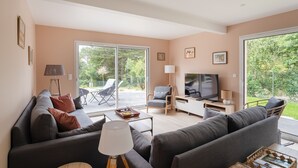 Ein modernes Wohnzimmer mit Sofa, Couchtisch, Fernseher und Blick ins Freie.