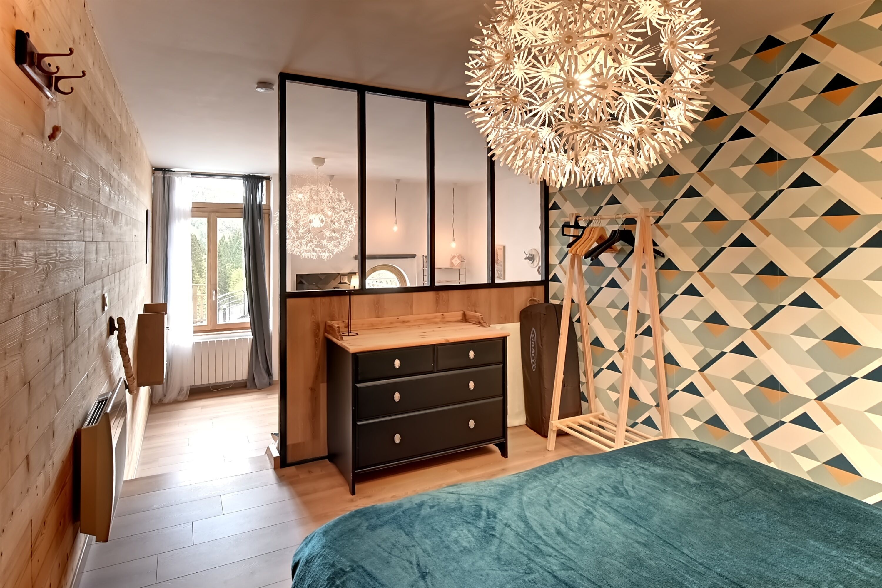 Un dormitorio moderno con una cama grande, un aparador de madera, una lámpara colgante y una pared con estampado geométrico.