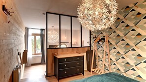 A modern bedroom with a large bed, a wooden dresser, a hanging light fixture, and a geometric-patterned wall.