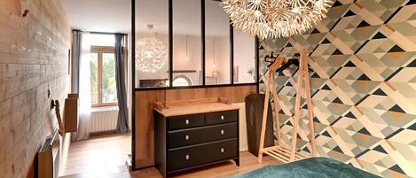 Un dormitorio moderno con una cama grande, un aparador de madera, una lámpara colgante y una pared con estampado geométrico.