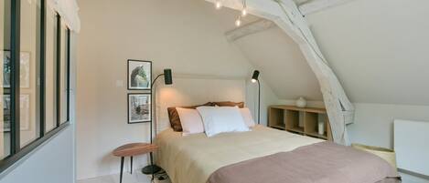 A bedroom with a bed, bedside tables, a nightstand, a lamp, and a window.