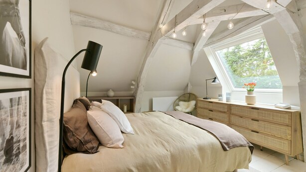 Une chambre à coucher comprenant un lit, une table de chevet, une lampe, une commode et une fenêtre donnant sur un paysage verdoyant.