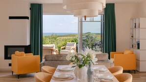 Ein modernes Wohnzimmer mit Essbereich, großen Fenstern mit Vorhängen und Blick ins Freie.