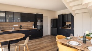 Eine moderne Küche mit dunklen Schränken, einem Holztisch und einer Treppe.