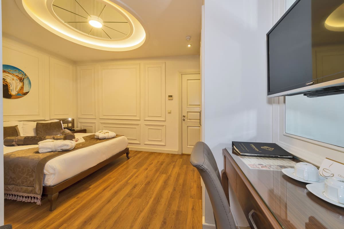 A hotel room with a bed, a desk with a computer, a television, and a painting on the wall.