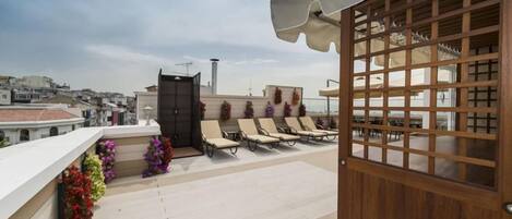 A rooftop terrace with sun loungers, a wooden gate, and a view of the cityscape.