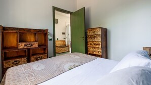 A bedroom with a bed, wooden dresser, and a green door leading to another room.