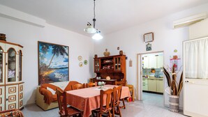 A dining area with a table set for four, surrounded by wooden chairs. A large painting of a beach scene hangs on the wall.