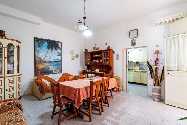 A dining area with a table set for four, surrounded by wooden chairs. A large painting of a beach scene hangs on the wall.