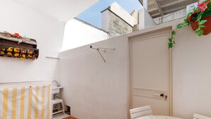 A small, clean bathroom with a sink, a toilet, and a shower area. There is a small table with a chair and a potted plant.