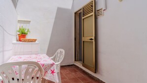 Une petite terrasse extérieure avec une table et des chaises, un pot de fleurs et une porte avec une fenêtre.