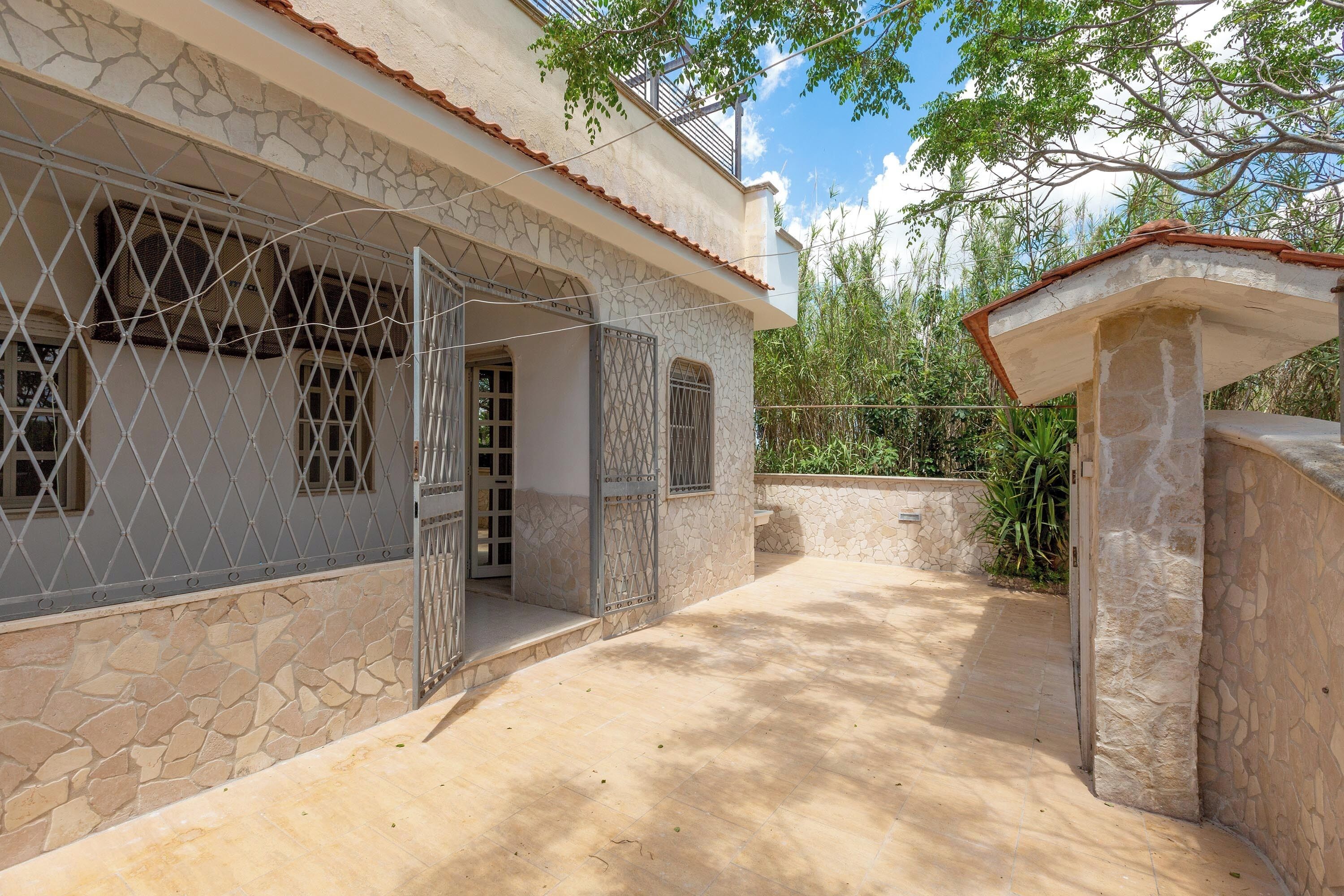 Une maison avec une façade en pierre, un patio carrelé et un portail en métal.