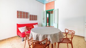 Uma sala de jantar com uma mesa redonda, cadeiras, um sofá vermelho e duas decorações de parede estampadas.