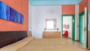 Um quarto com cama, penteadeira, espelho e uma cadeira vermelha.
