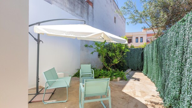 Área de pátio com um guarda-sol branco, duas cadeiras verdes e piso de concreto.