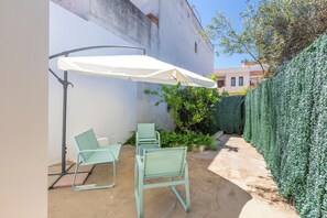 Un espace patio avec un parasol blanc, deux chaises vertes et un sol en béton.
