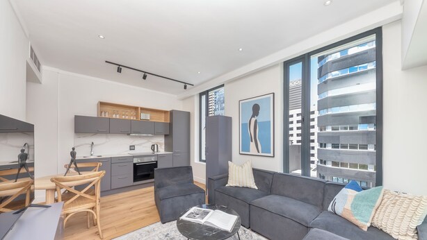 Een moderne woonkamer met een grijze bank, een salontafel en een eethoek met een houten tafel en stoelen.