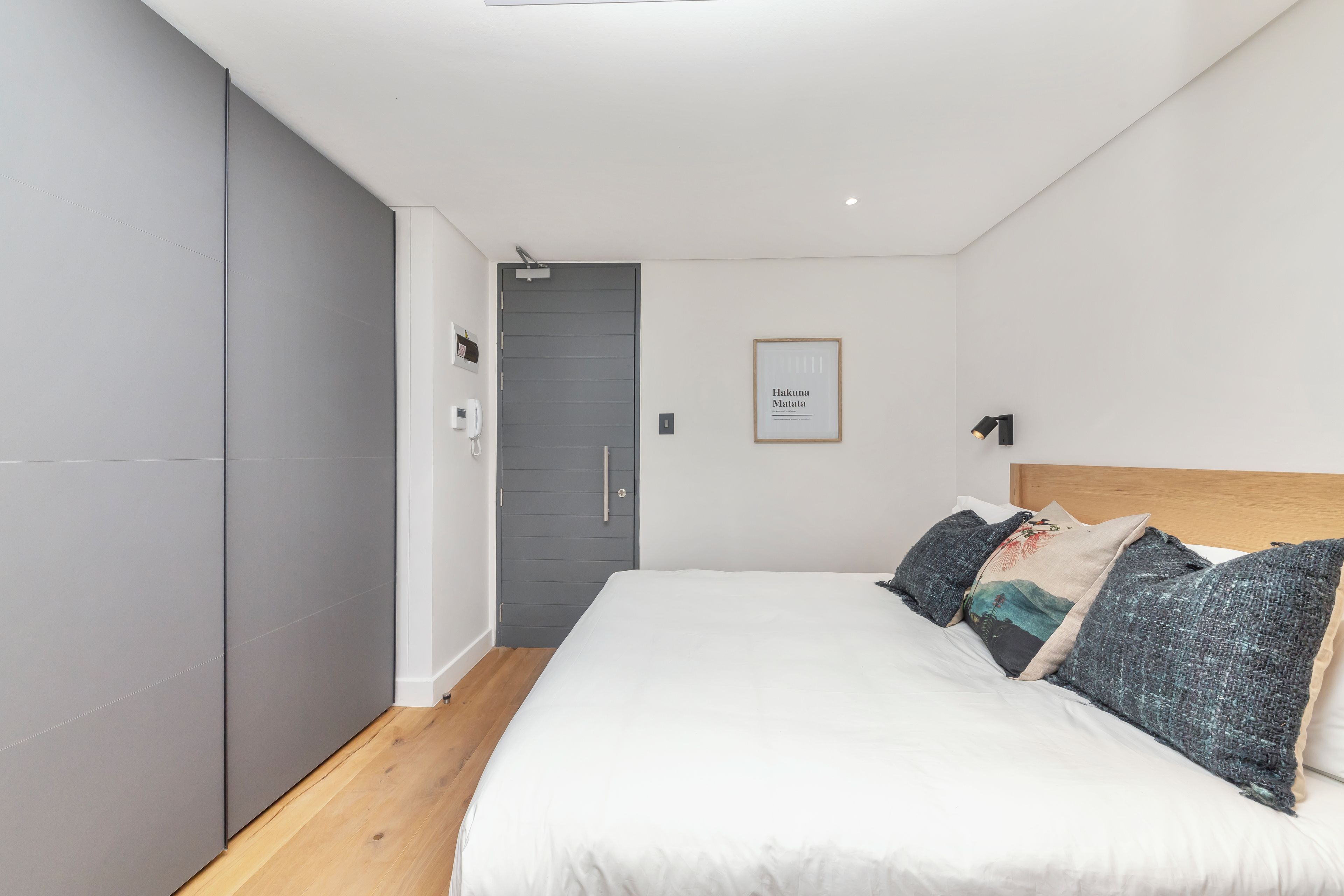 A modern bedroom with a large bed, grey wardrobe, and a framed artwork on the wall.