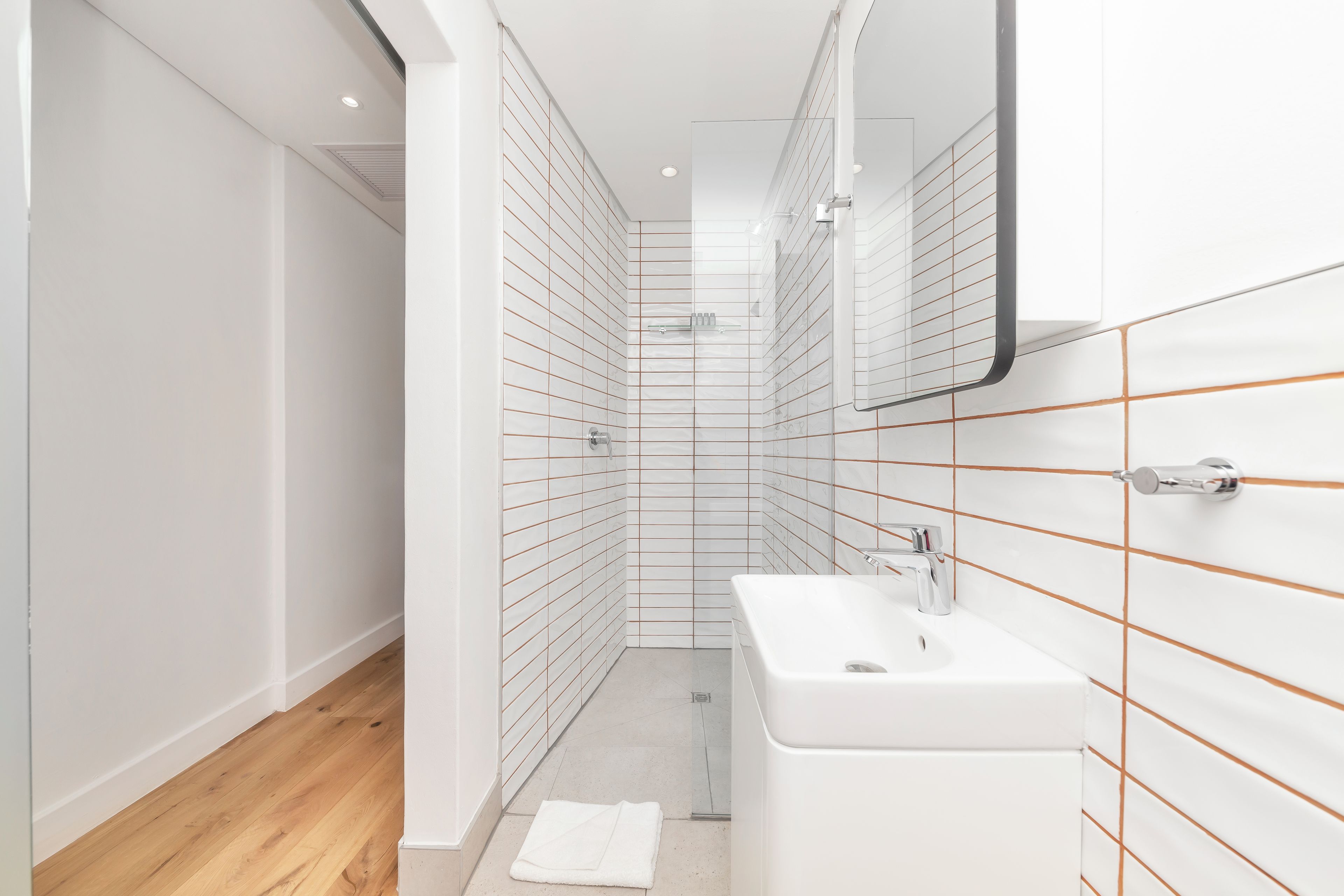 A modern bathroom with white tiles, a wooden floor, and a white sink.