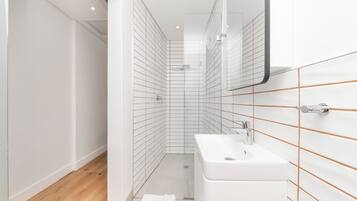 A modern bathroom with white tiles, a wooden floor, and a white sink.