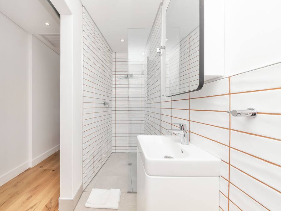 A modern bathroom with white tiles, a wooden floor, and a white sink.